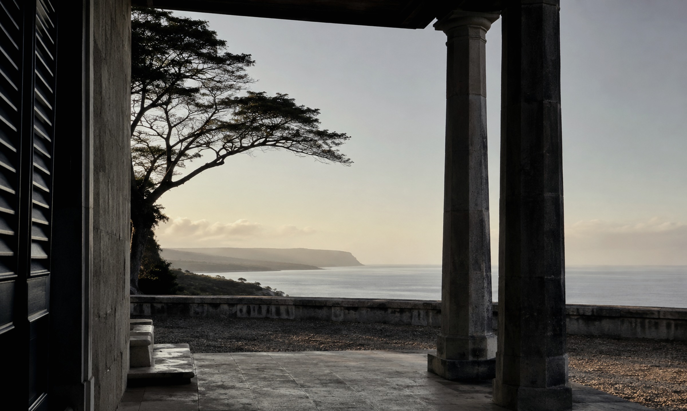 Editorial study of a shaded stone veranda opening onto a calm sea and distant headland.